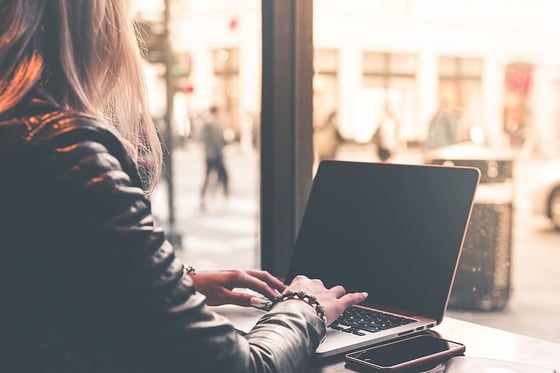Blonde woman typing away on laptop in a Cafe.
